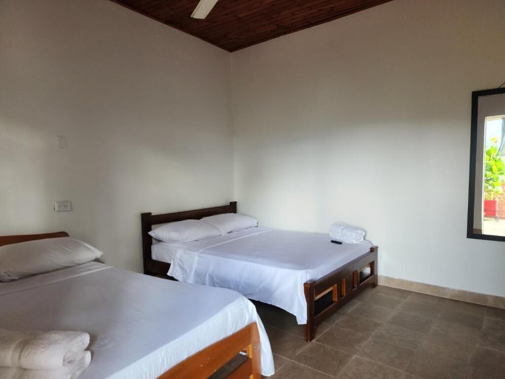 A room with two single beds, wooden headboards, white linens, and a window with a view of greenery.