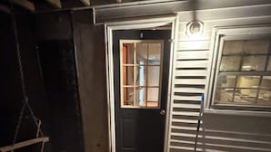 Ein Zimmer mit einer schwarzen Tür, einem Fenster und einem an der Wand angelehnten Besen.