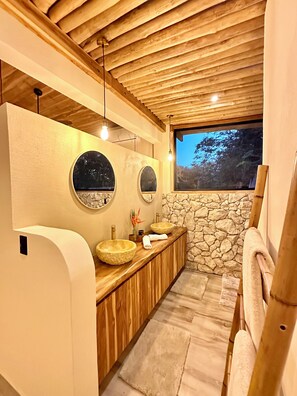 Ein modernes Badezimmer mit Holzbalken, Steinwänden und zwei runden Spiegeln.
