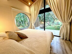 Ein Schlafzimmer mit einem großen Bett, einem Rundfenster und Blick auf einen Garten.