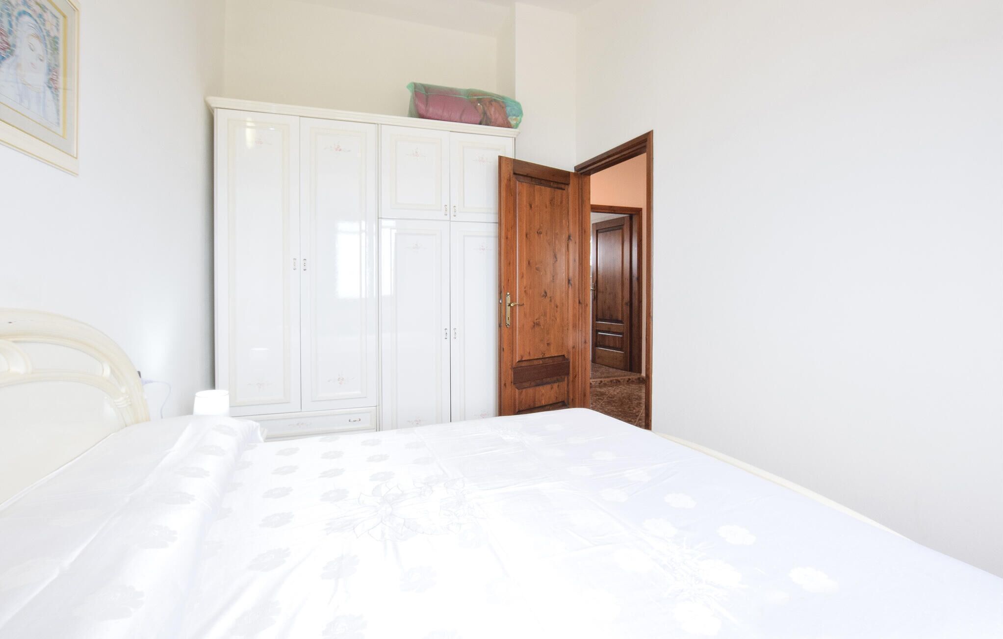 A bedroom with a bed, a white wardrobe, and a wooden door leading to another room.