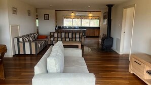 Una sala moderna con un sofá blanco, un sofá a rayas y una mesa de centro de madera. Hay una zona de cocina con estufa y ventana.