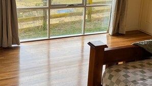 Un dormitorio con un ventanal grande, suelo de madera y una cama con colcha a cuadros.