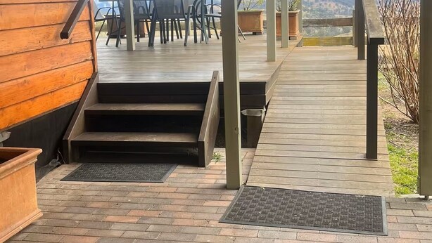 Un espacio al aire libre cubierto con una terraza de madera, escalones que conducen a un patio y vistas a montañas.