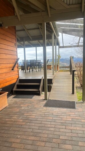 A covered outdoor area with a wooden deck, steps leading to a patio, and a view of mountains. - Farmhouse Chaplow - Feel at peace with the world at this tranquil getaway. (Megalong Valley)