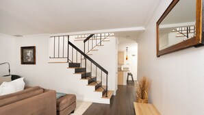 Un salon moderne avec un canapé marron, une table basse en bois et un escalier menant à un espace cuisine.
