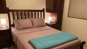 Una cama bien hecha con una manta color turquesa, cabecera de madera y dos lámparas de noche.