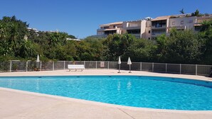 En swimmingpool med et hvidt hegn, en bænk og parasoller.