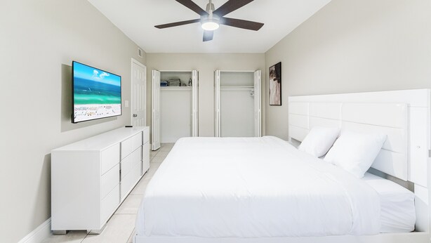 A bedroom with a bed, a ceiling fan, a TV, and a white wardrobe. - Modern Boca Condo Near FAU : 2 KING BR + Pool (Boca Raton)