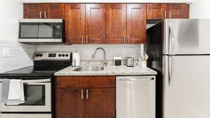 A modern kitchen with wooden cabinets, stainless steel appliances, a granite countertop, and a built-in oven. - Modern Boca Condo Near FAU : 2 KING BR + Pool (Boca Raton)