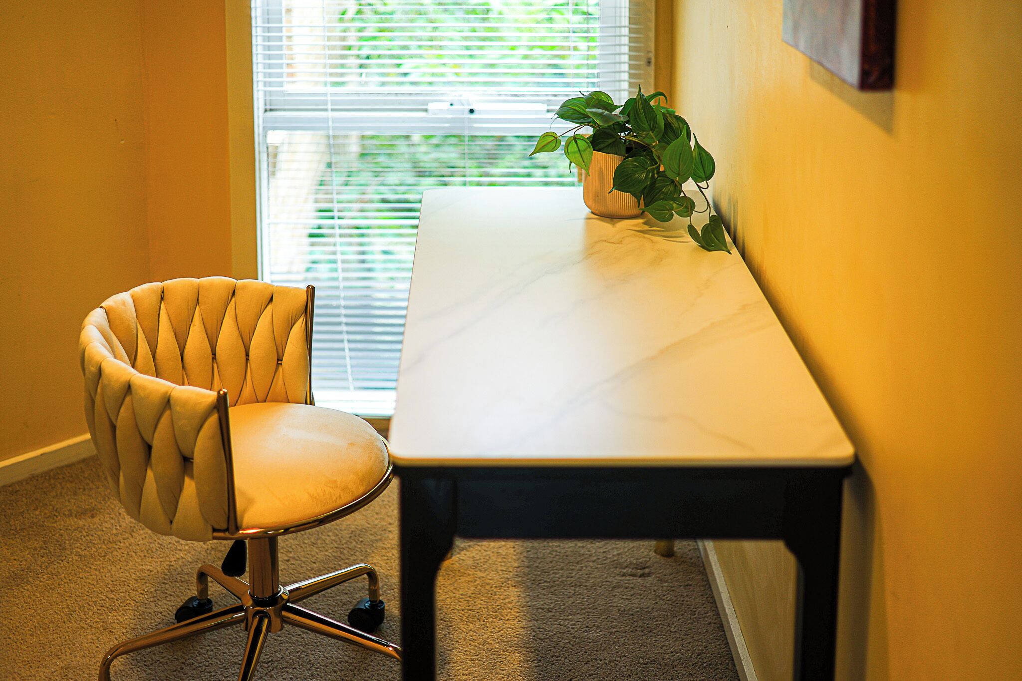 Oficina en esquina con sillón acolchado, una mesa blanca y una planta en maceta.