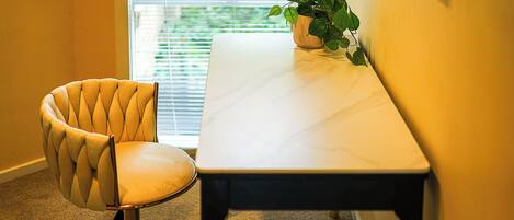 Oficina en esquina con sillón acolchado, una mesa blanca y una planta en maceta.