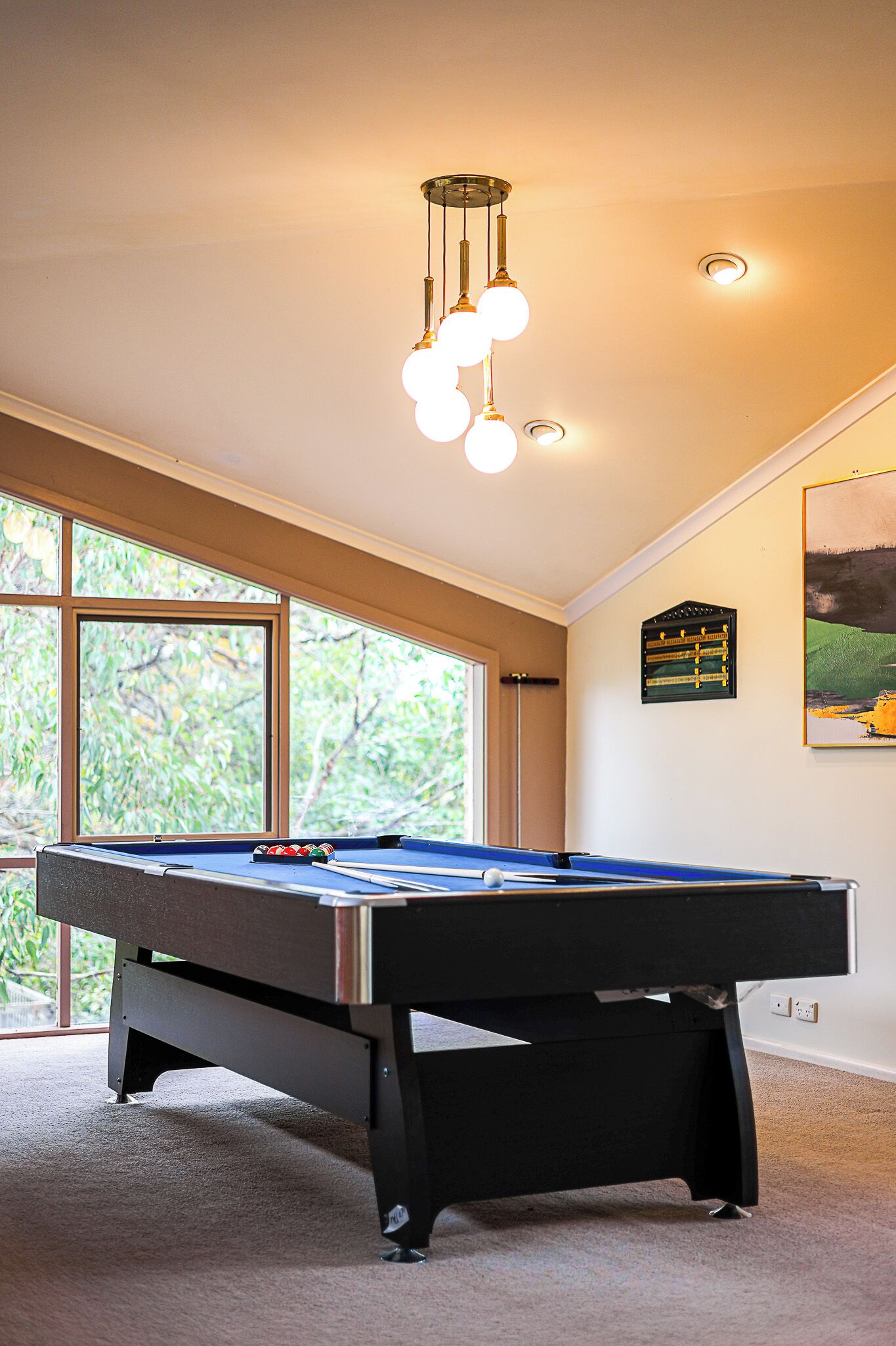 A pool table in a room with large windows, a ceiling light fixture, and a framed picture on the wall.