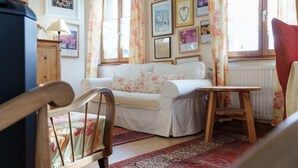 A cozy room with a wooden chair, a white sofa, a small table, and a red patterned rug. - Sévilla Guest Room in Boersch with Garden View (Boersch)