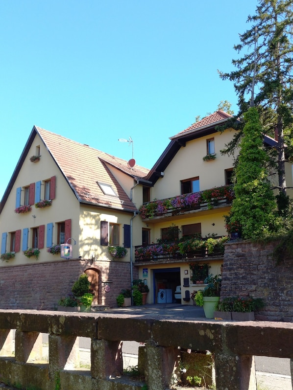 A traditional European-style building with a stone facade, multiple balconies with flower boxes, and a clear blue sky. - Delphi Guest Room with Mountain View (Boersch)