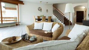 Un salon accueillant avec un canapé en osier, une table à manger avec des chaises, un escalier et une lampe.