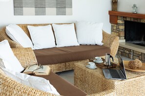 Ein Rattansofa mit weißen Kissen, ein Laptop, eine Tasse und ein Buch auf einem gewobenen Hocker.