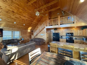 A spacious cabin with a loft bedroom, a living area with a sofa and coffee table, and a kitchen with wooden cabinets and appliances. - The Overlook at Grouse Ridge (Sevierville)
