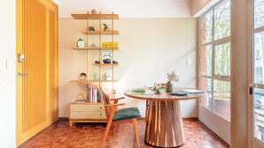 A room with a wooden floor, a round wooden table with a chair, a bookshelf, and a window with a view of trees. - Roma Norte - Sunny and Mid-Century Modern Casa Apache (Ciudad de México)