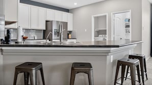 Una cucina moderna con mobili bianchi, una grande isola con sgabelli, elettrodomestici in acciaio inossidabile e luci a incasso nel soffitto.