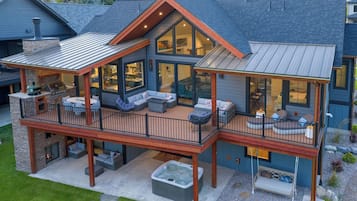 A two-story house with a covered deck, outdoor seating, and a hot tub.