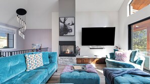 Ein modernes Wohnzimmer mit Kamin, einem großen Flachbildfernseher und Blick ins Freie.