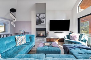 Un salon moderne doté d’une cheminée, d’un grand téléviseur à écran plat et offrant une vue sur l’extérieur.