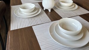 A dining table set with white plates and bowls, a potted plant, and a television in the background.