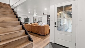 A modern kitchen with a central island, a dining area with a brown sofa, and a staircase leading to a second floor. - Retreat home tucked away in the forest, perfect for big groups, near Bass Lake (Oakhurst)