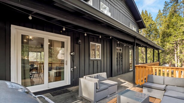 A modern outdoor deck with a covered seating area, a wooden deck, and a glass door leading to an interior space. - Retreat home tucked away in the forest, perfect for big groups, near Bass Lake (Oakhurst)