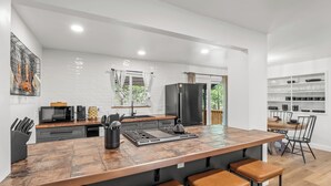 A modern kitchen with a central island, bar stools, and a dining area with a wooden table and chairs. - Retreat home tucked away in the forest, perfect for big groups, near Bass Lake (Oakhurst)