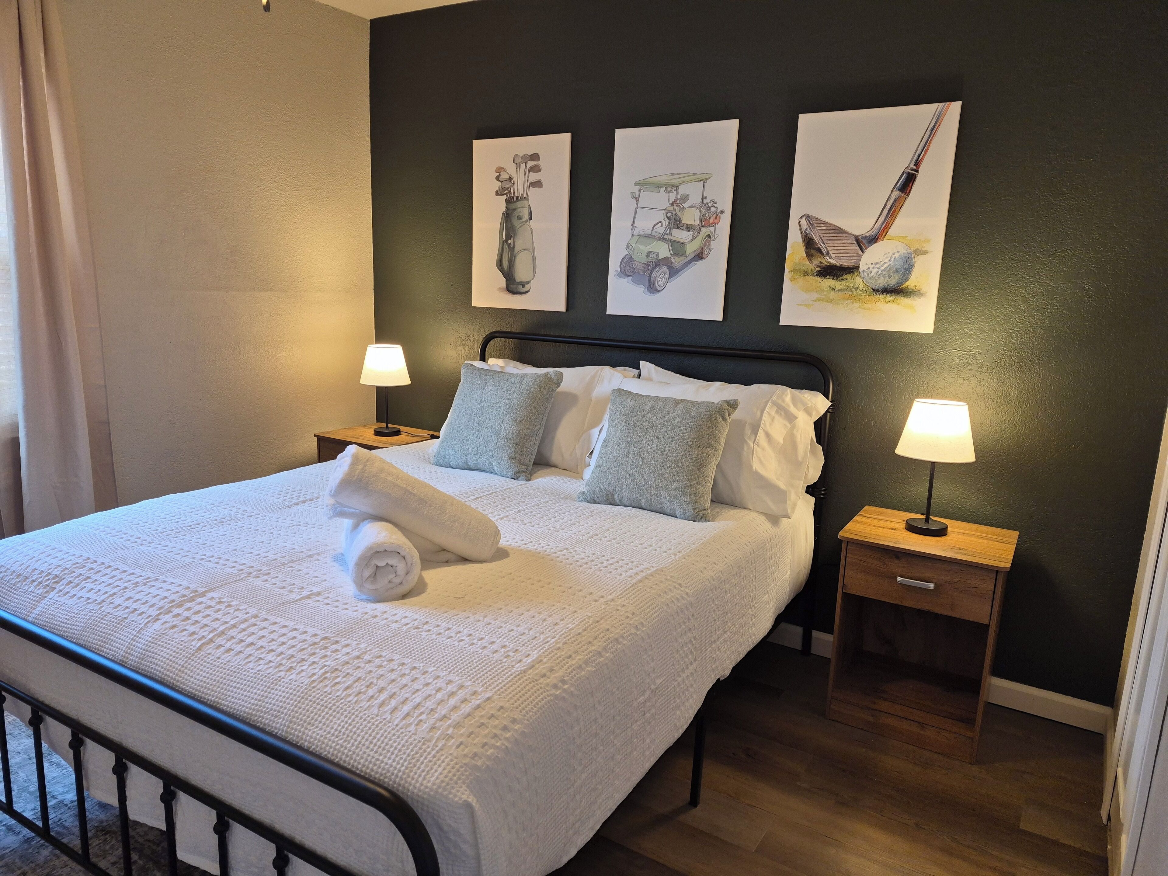 A neatly made bed with a rolled towel, two pillows, and a bedside lamp on a wooden nightstand.