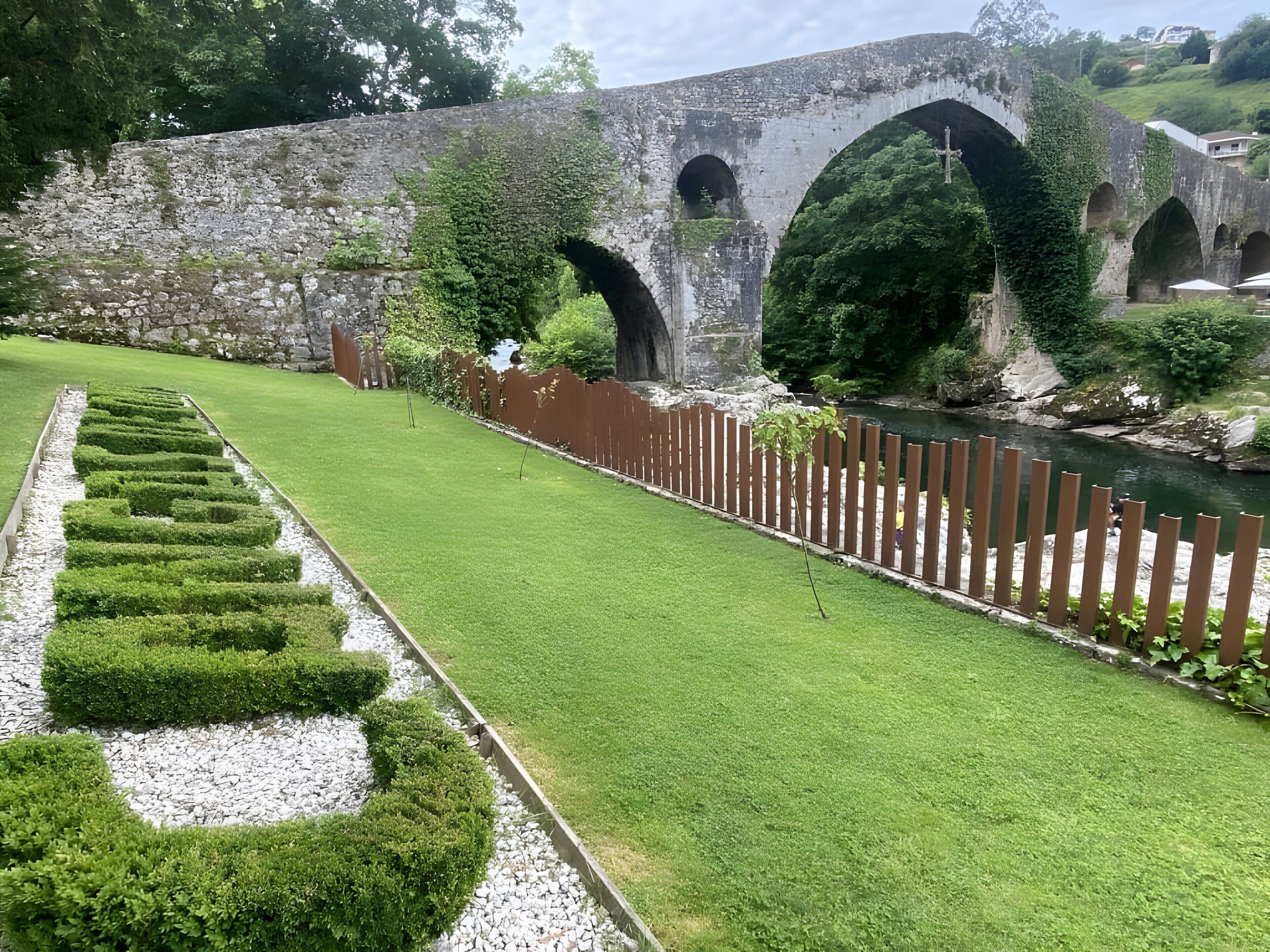 A stone bridge with arches, a well-maintained lawn, and a river.