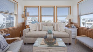 Ein gemütliches Wohnzimmer mit einem beigefarbenen Sofa, einem Glastisch und Blick auf die Stadt durch große Fenster.