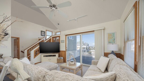 Ein geräumiges Wohnzimmer mit einem großen Flachbildfernseher, einer Holztreppe und einem Balkon mit Blick auf die Stadt.