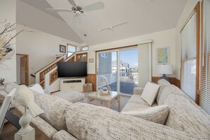 Ein geräumiges Wohnzimmer mit einem großen Flachbildfernseher, einer Holztreppe und einem Balkon mit Blick auf die Stadt.