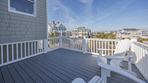 Eine Holzterrasse mit weißen Geländern, einem Stuhl und Blick auf Häuser im Hintergrund.