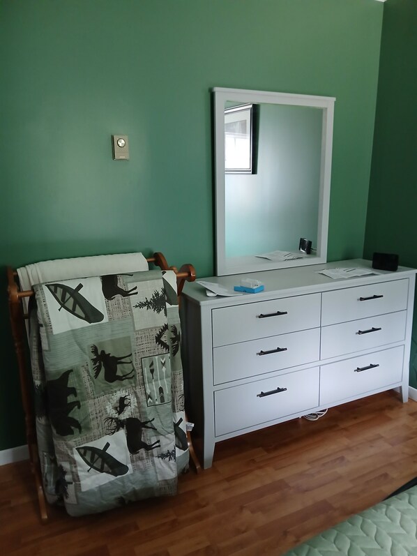 A bedroom with a wooden chair, a white dresser with drawers, a mirror, and a green wall.