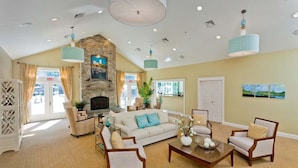 A spacious lobby with a high ceiling, a stone fireplace, and a large window. - Seaglass Village 805: Coastal Charm Cottage - Spacious Port Model w/ Resort Amenities (Wells)