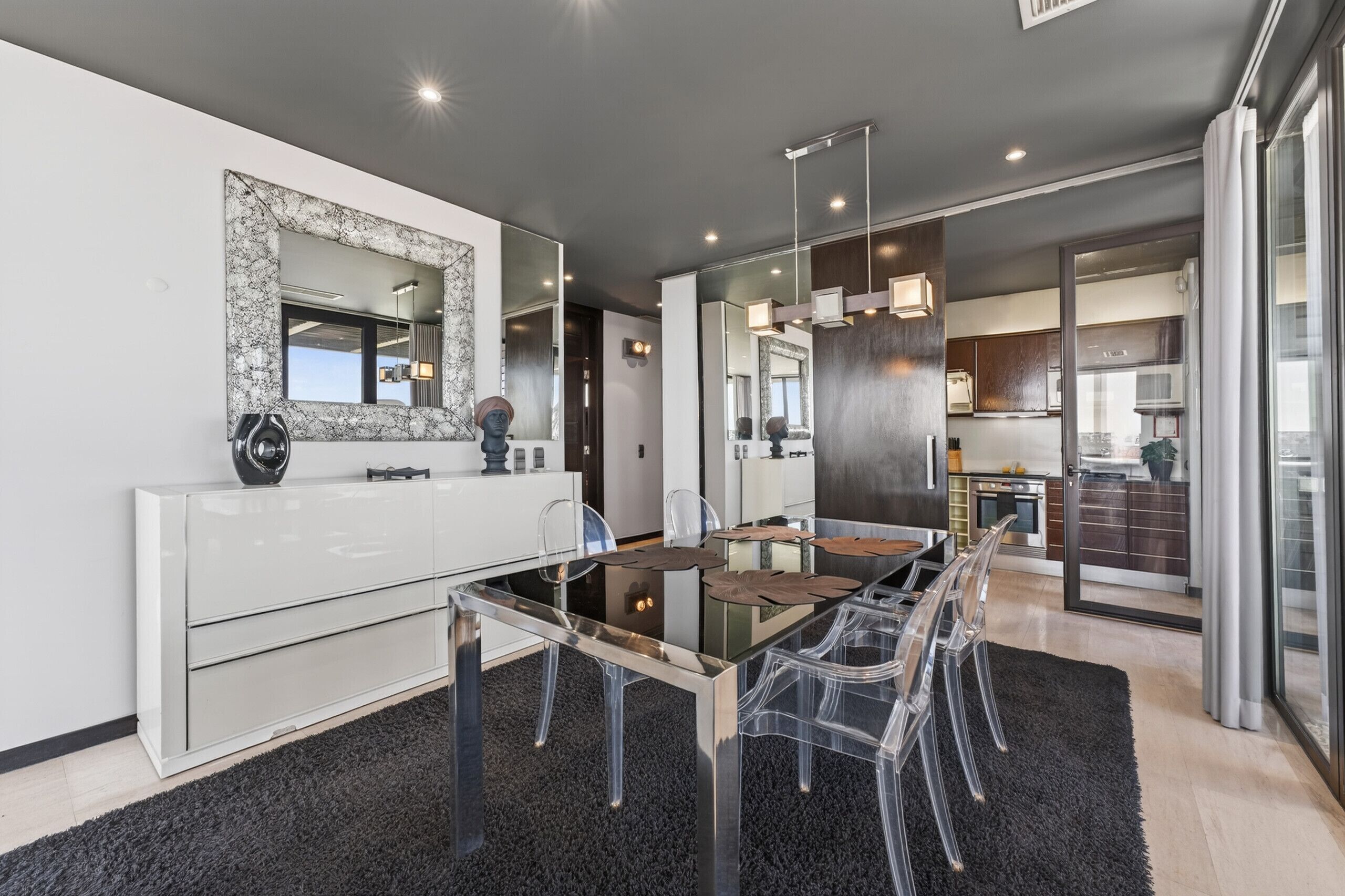 A modern kitchen with a large island, a dining area with a glass table and chairs, and a large mirror on the wall.