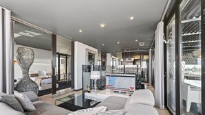 A modern living room with a sofa, a large vase, a TV, and a glass partition. - Penthouse Grand Noir | Outdoor Jacuzzi | Near the Strip (Albufeira)