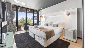 A modern bedroom with a large bed, a glass desk, and a view of palm trees. - Penthouse Grand Noir | Outdoor Jacuzzi | Near the Strip (Albufeira)