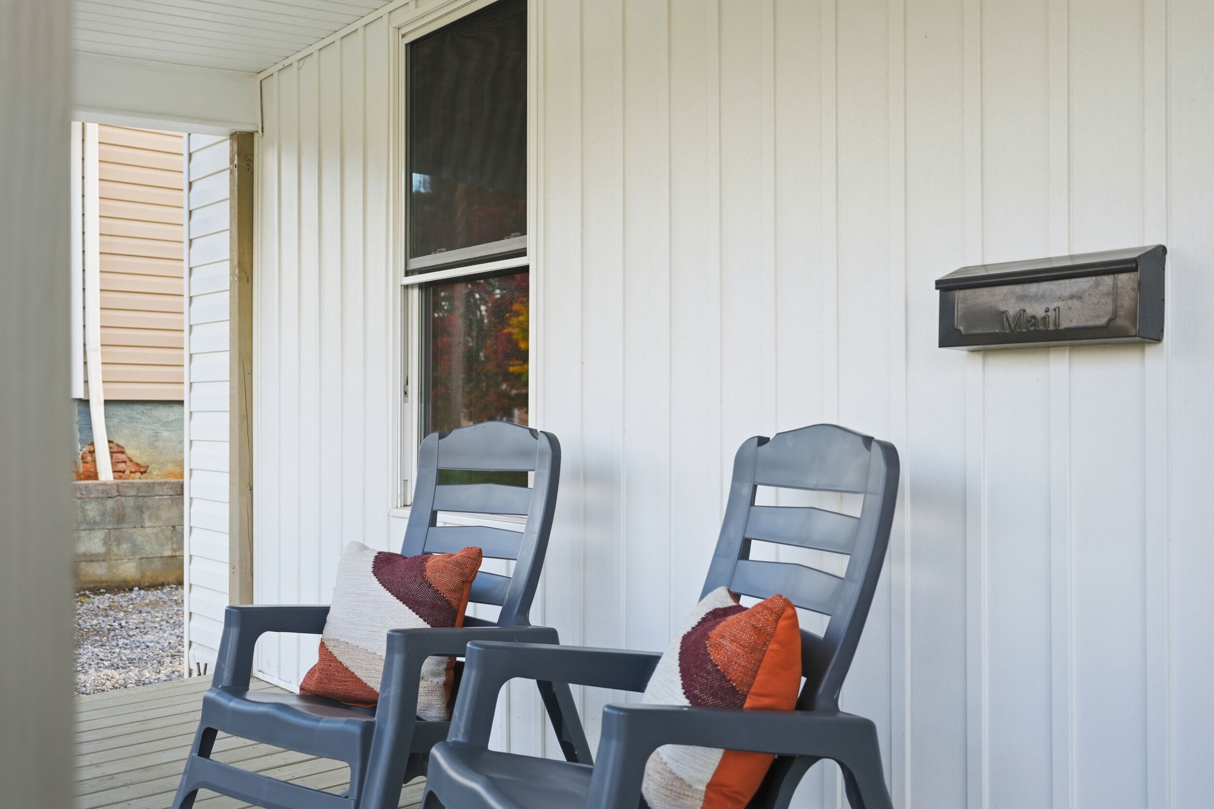 Two chairs with cushions outside a building with a mailbox on the wall.
