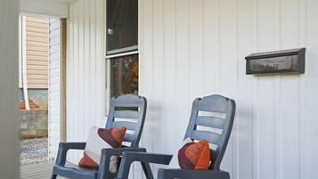 Two chairs with cushions outside a building with a mailbox on the wall.