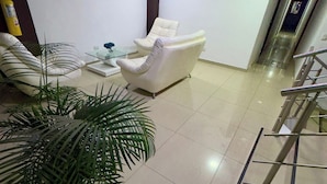 A modern living room with a flat-screen TV, a white sofa, a white armchair, and a coffee table. There are potted plants and a staircase leading to an upper floor. - Hotel Blue Santa Rosa de Cabal (Santa Rosa de Cabal)