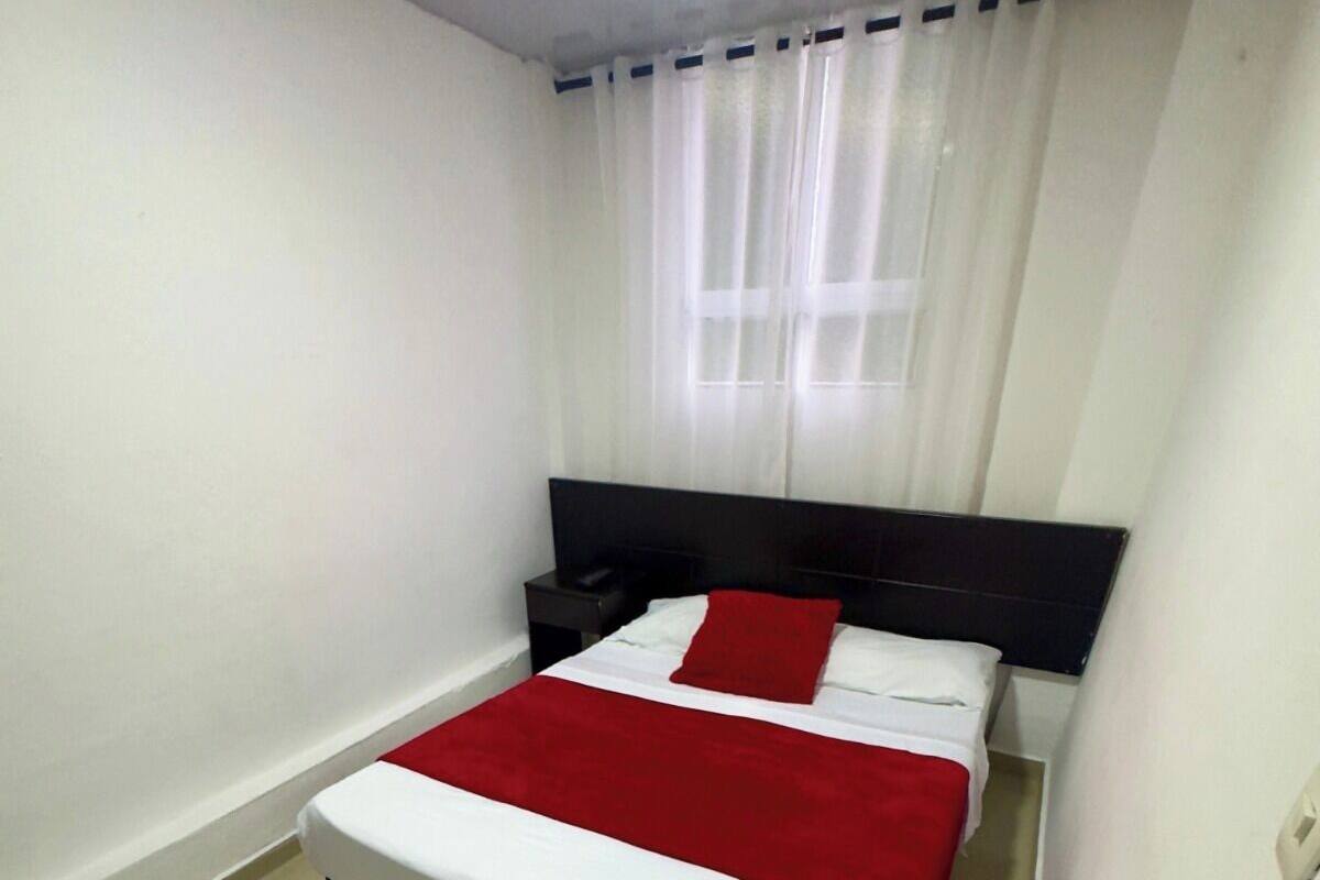 A bedroom with a bed, a nightstand, and a window with curtains.