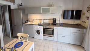 A compact kitchen with a washing machine, oven, microwave, and a dining area with a table and chairs. - Lovely semi-detached villa in residence with pool near Richelieu beach, Cap d'Agde (LE CAP D AGDE)