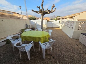 A patio with a round table covered by a green tablecloth, surrounded by white plastic chairs. - Lovely semi-detached villa in residence with pool near Richelieu beach, Cap d'Agde (LE CAP D AGDE)