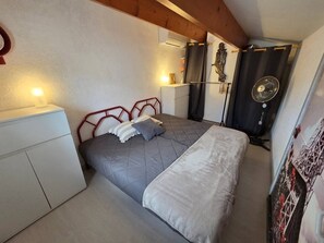 A bedroom with a bed, bedside table, and a fan. - Lovely semi-detached villa in residence with pool near Richelieu beach, Cap d'Agde (LE CAP D AGDE)