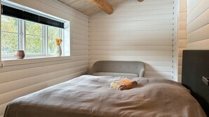 En säng för en person med en grå sänggavel i ett rum med vitmålade panelväggar och ett fönster med utsikt över träd.